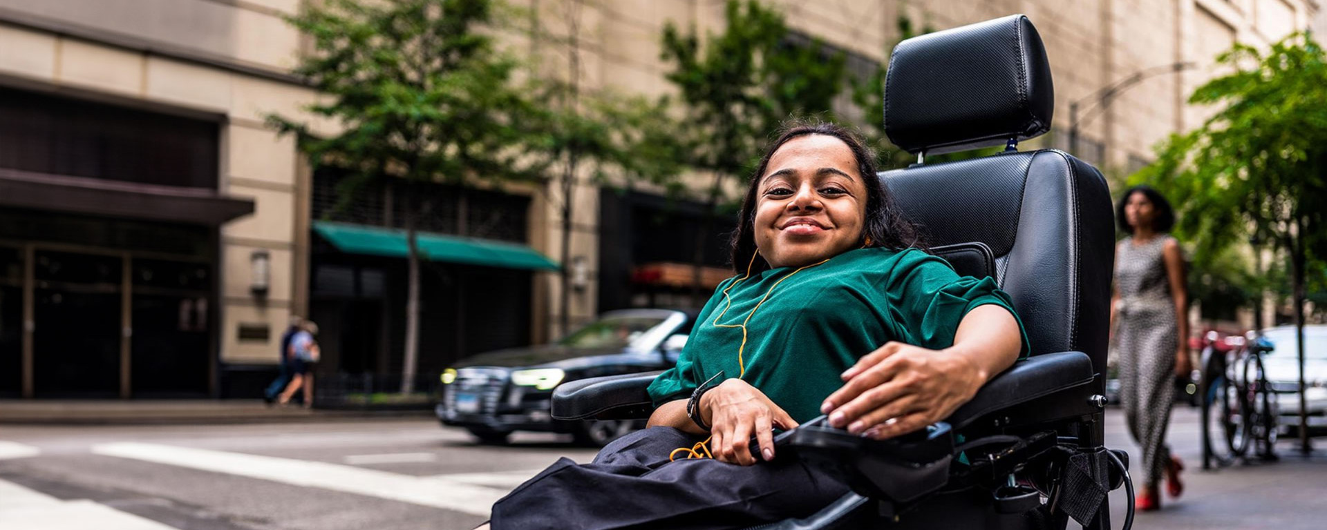 Disabled woman in motorized wheelchair on sidewalk smiling.