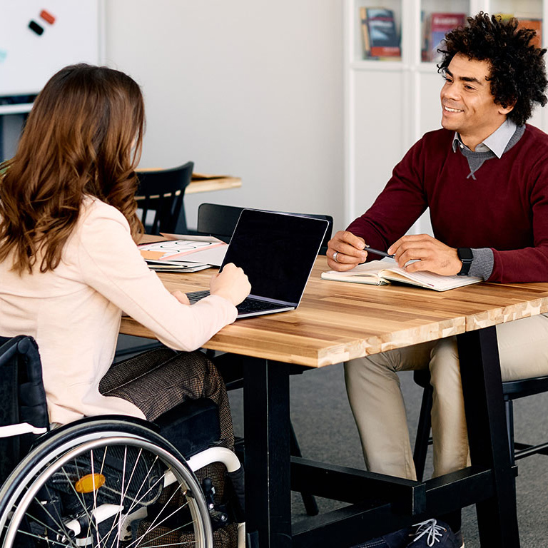 A disabled female employee in wheelchair is working with a male employee with a service dog.