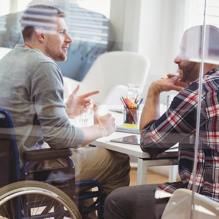Two male co-workers are collaborating in a conference room. One disabled male is in a wheelchair.
