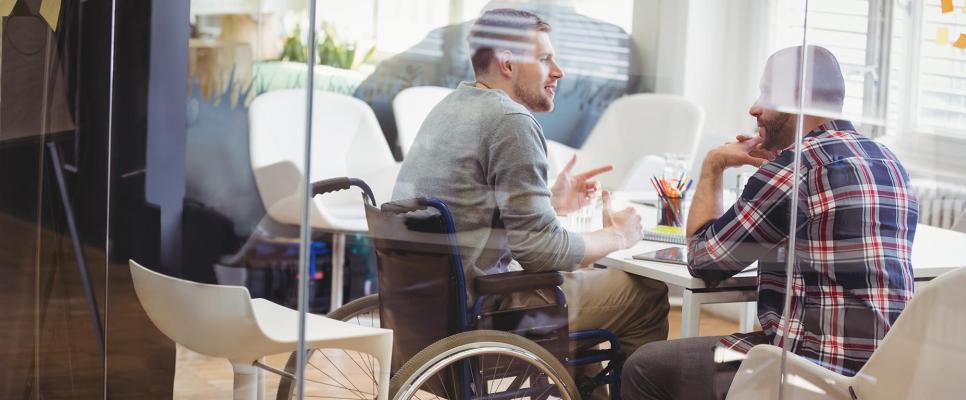 Two men, one in a wheelchair, meeting in a conference room.